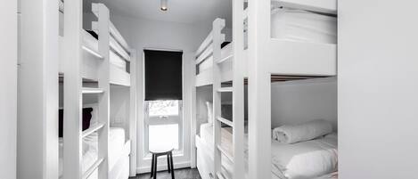 A narrow, white, walk-in closet with multiple shelves and a small stool in the center.