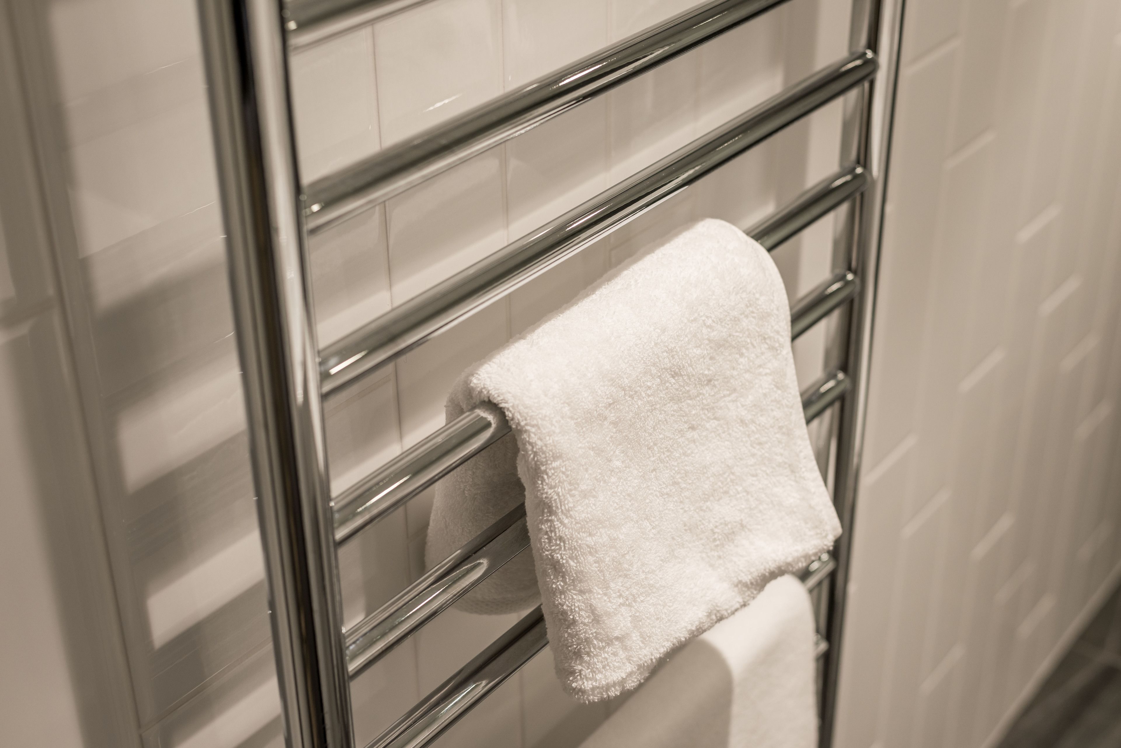 A white towel hanging on a chrome towel rack in a bathroom with tiled walls.