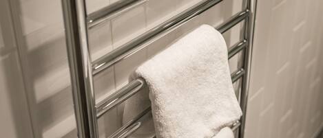 A white towel hanging on a chrome towel rack in a bathroom with tiled walls.