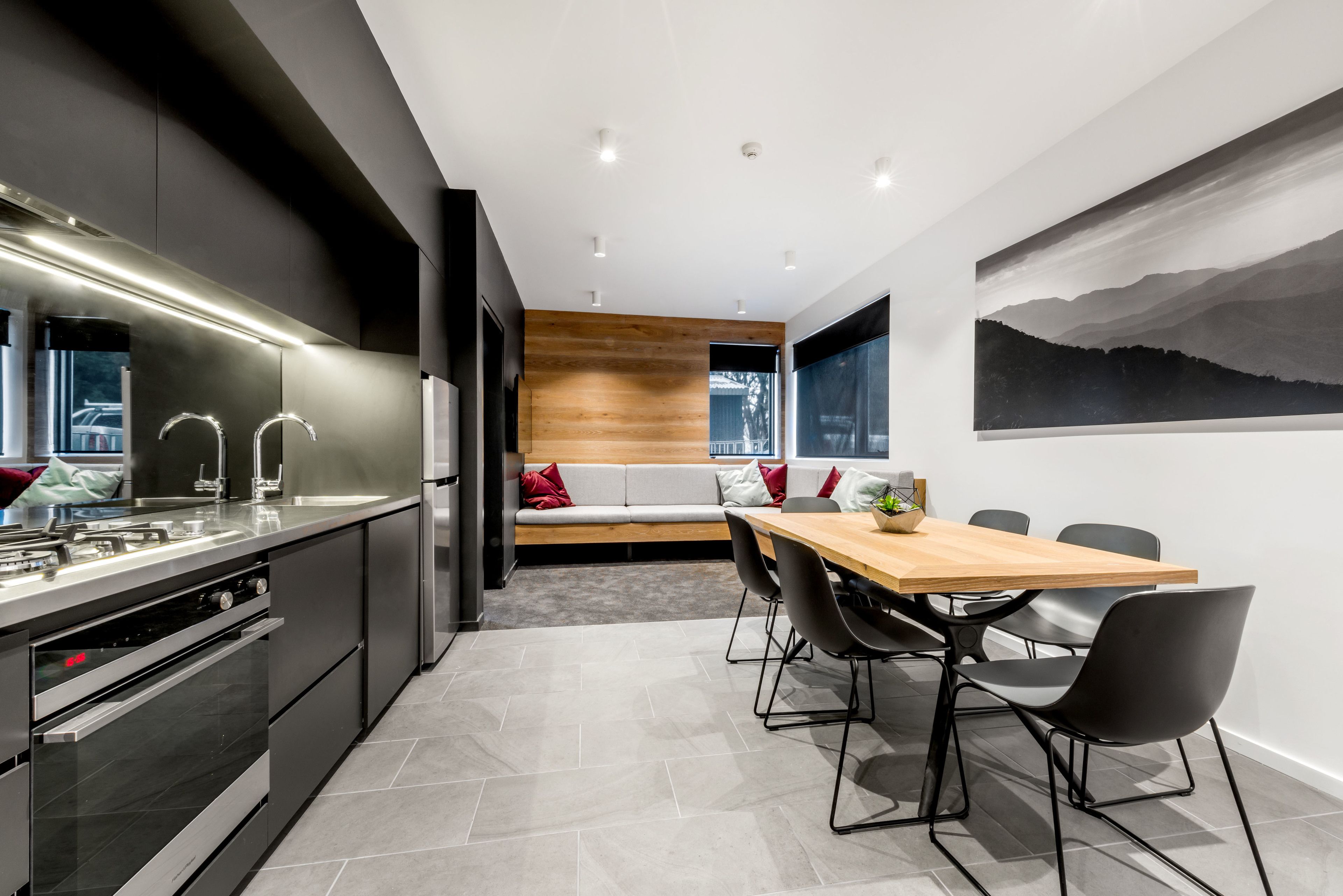 A modern kitchen with a built-in oven and a dining area with a wooden table and black chairs.