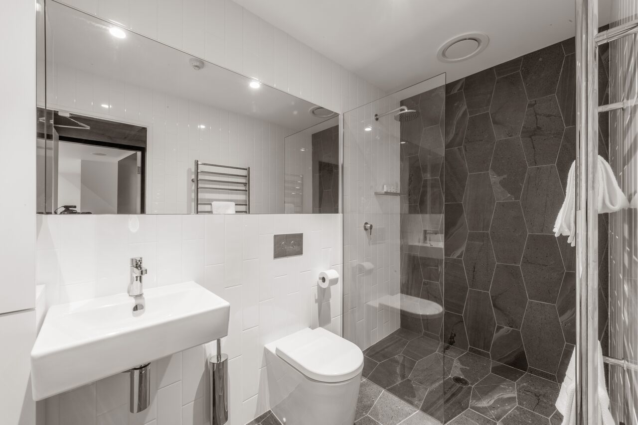 Un bany modern amb un lavabo blanc, vàter i box de dutxa de vidre.