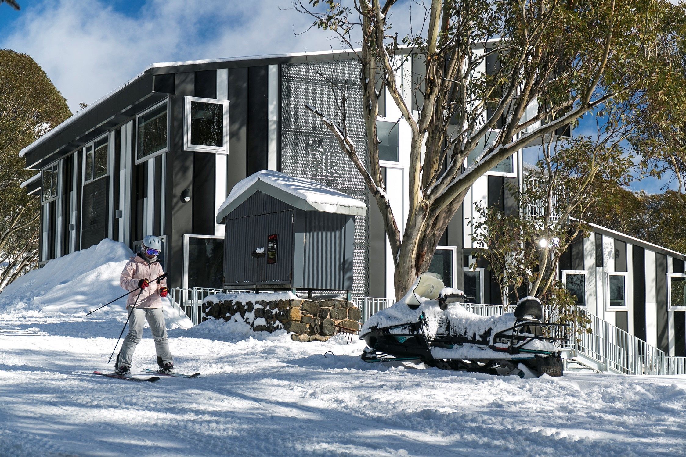 Un edificio moderno con base de piedra y techo cubierto de nieve.