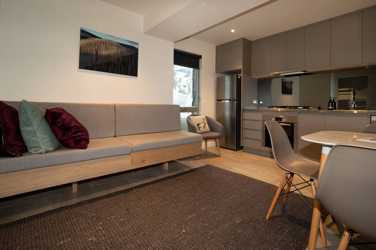 A modern kitchen with grey cabinets, a stainless steel refrigerator, and a dining area with a table and chairs.