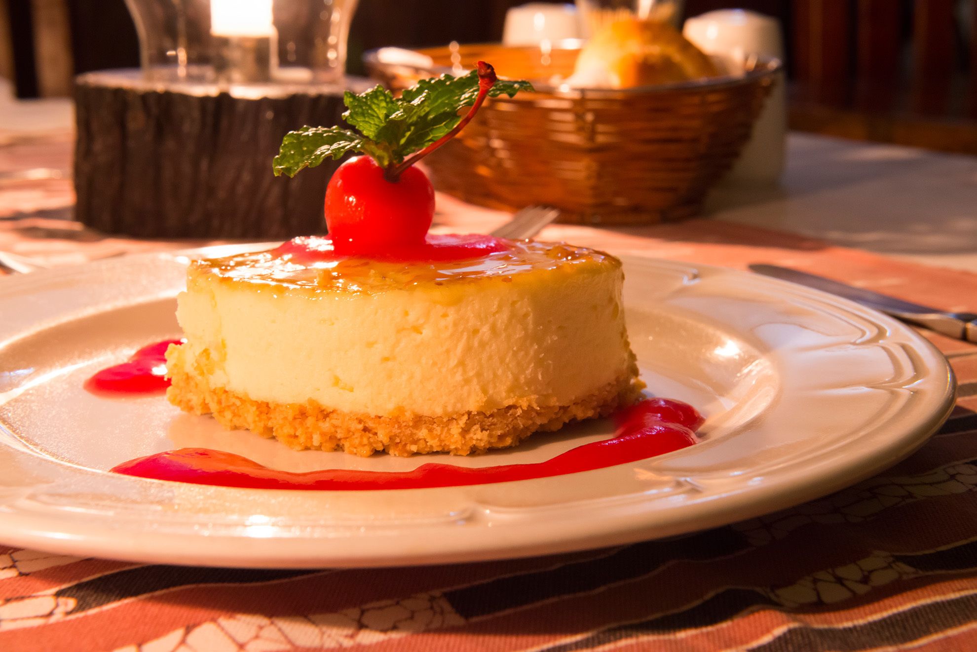 A cheesecake on a white plate with a red berry on top, surrounded by a red sauce.