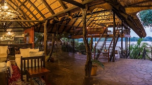 Un interior rústico con techo de paja, muebles de madera, zona de bar y vistas al exterior.