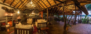 A rustic interior with a thatched roof, wooden furniture, a bar area, and a view of the outdoors.