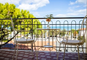 A balcony with two metal chairs and a small table, a vase with flowers, and a view of the sea. - Hotel Stella (Riccione)
