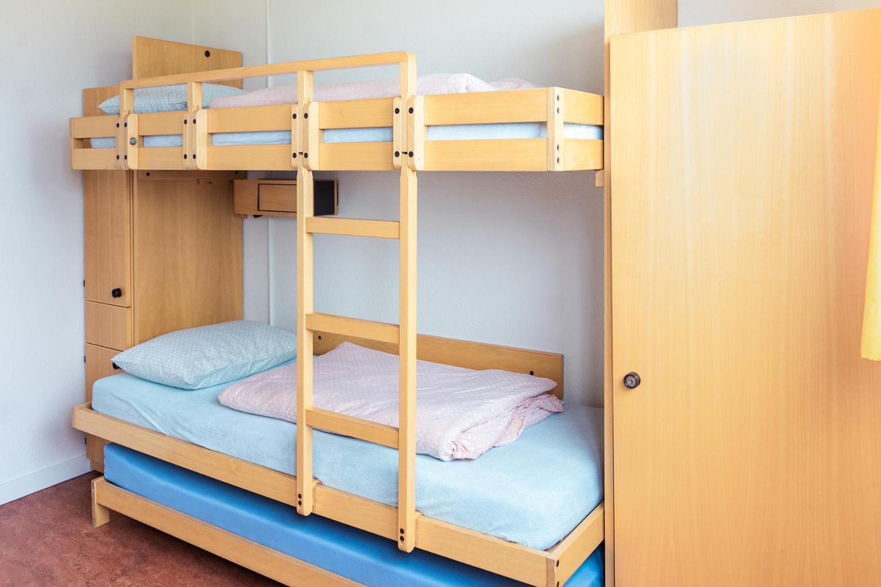 Cama litera con una cama inferior y una superior, ambas con ropa de cama azul. A la derecha, un armario de madera.