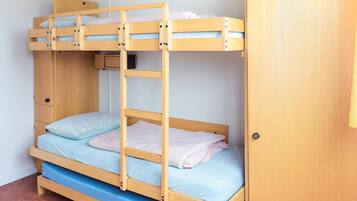 Cama litera con una cama inferior y una superior, ambas con ropa de cama azul. A la derecha, un armario de madera.