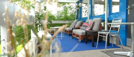 Un espace extérieur abrité, avec un sol bleu, deux canapés avec des coussins, une petite table et des chaises.