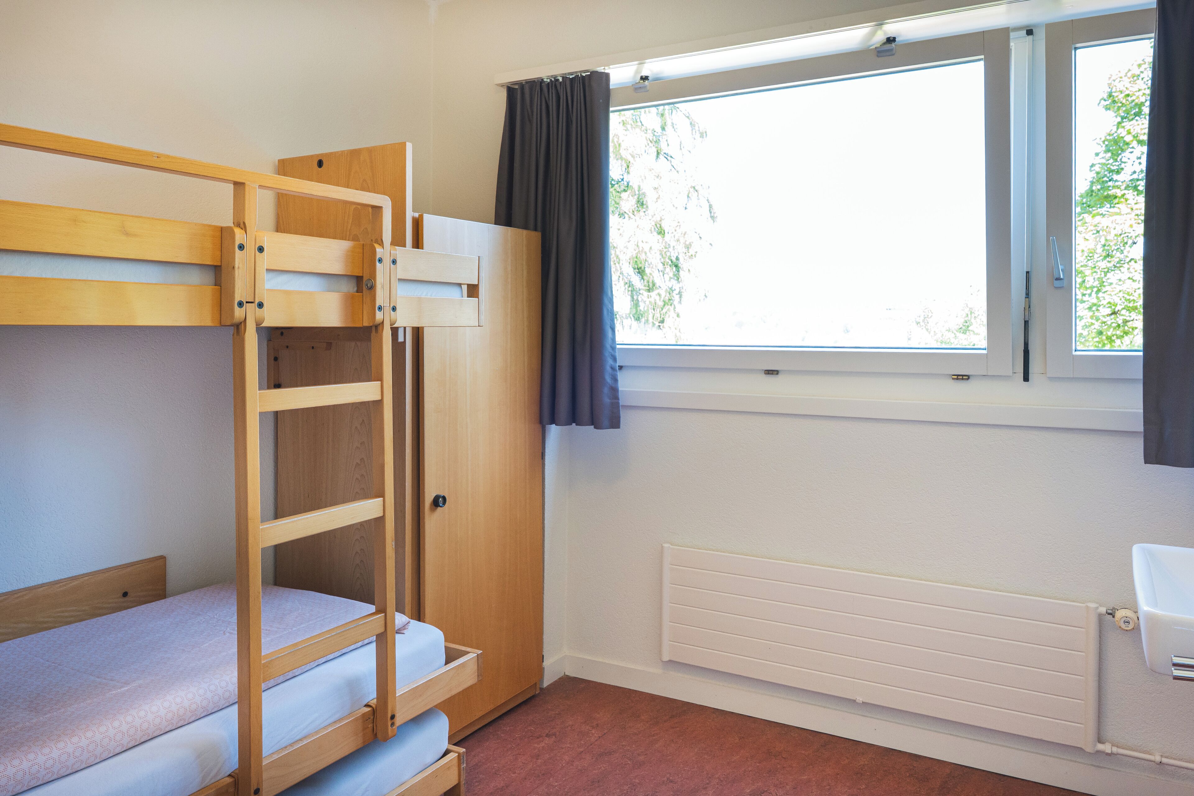 A bunk bed room with a window, radiator, and a door.