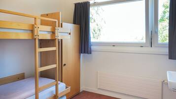 A bunk bed room with a window, radiator, and a door.