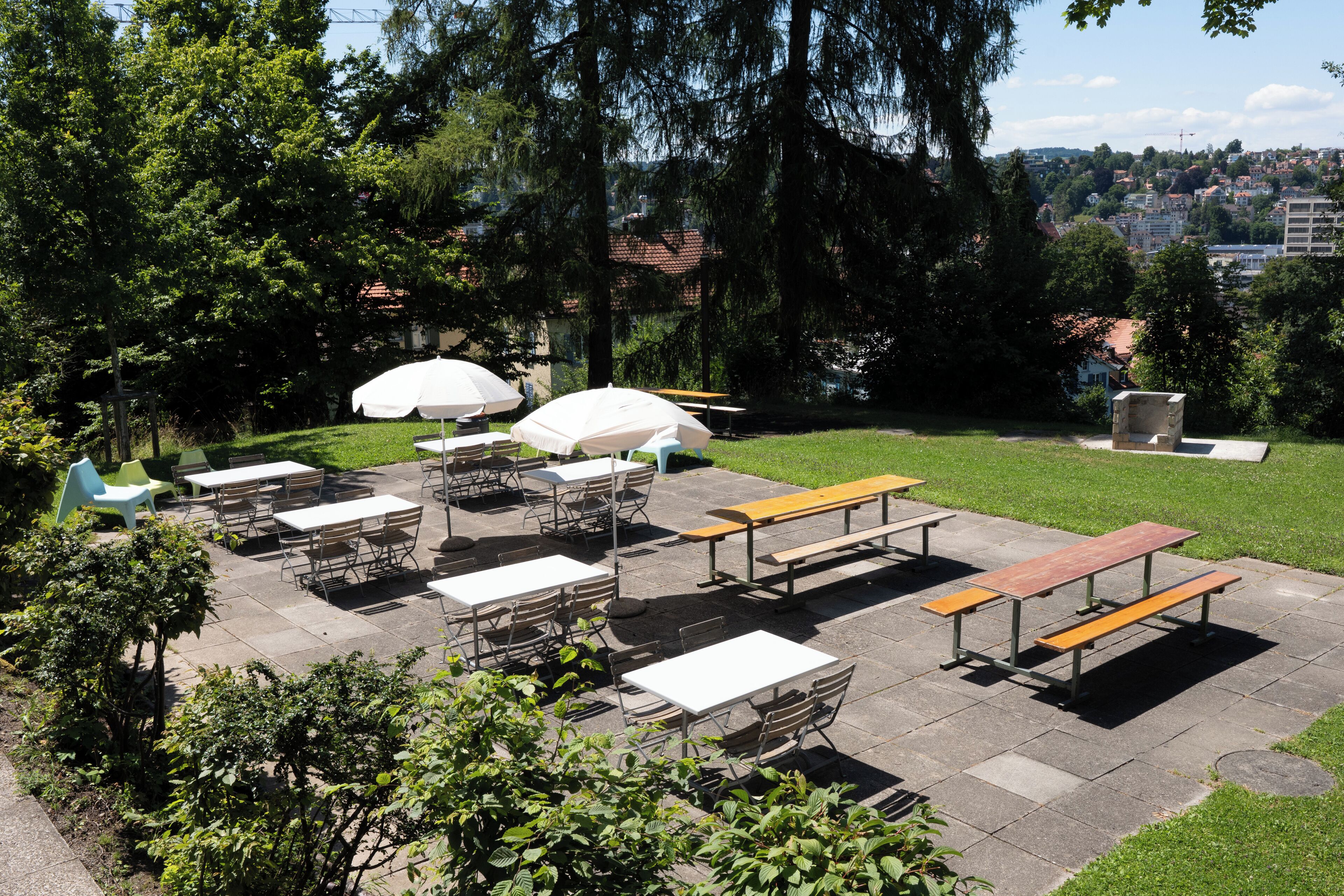 Un patio al aire libre con mesas y bancos, rodeado de follaje y árboles.