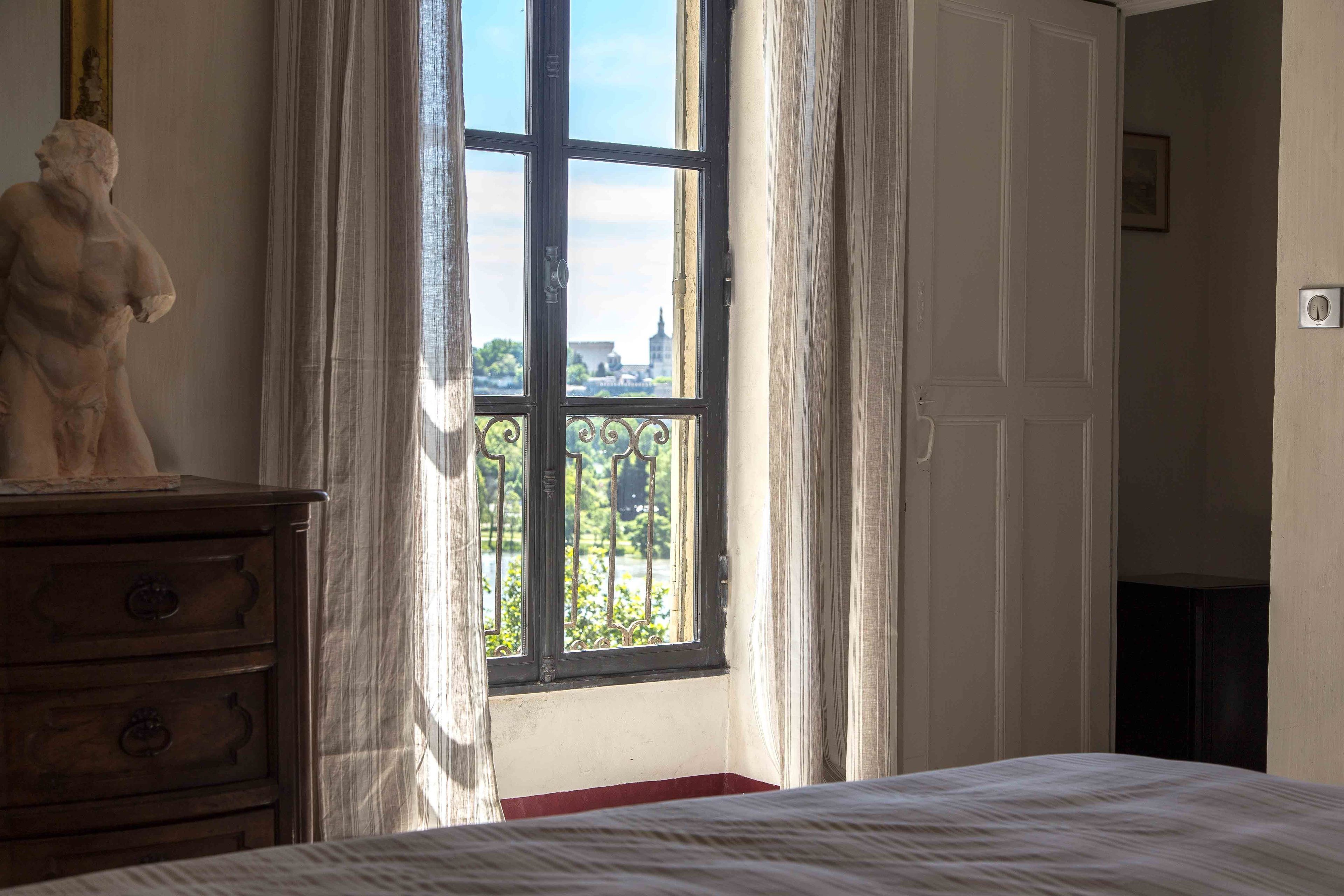 Una habitación con una cama, un aparador y un ventanal con cortinas.