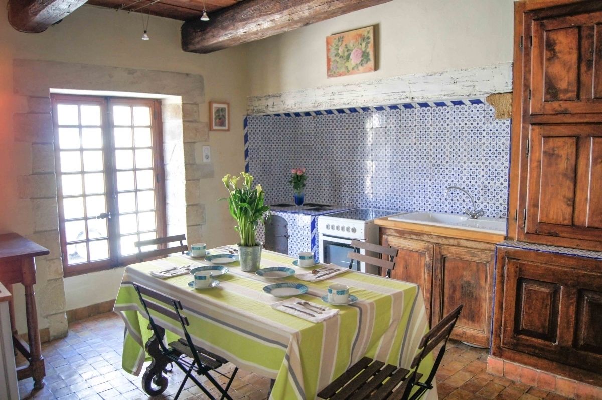 A rustic kitchen with a tiled backsplash, wooden cabinets, and a dining area with a table set for two.