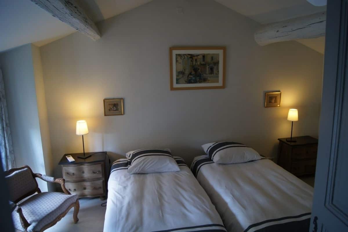 Een hotelkamer met twee eenpersoonsbedden, een houten stoel, een nachtkastje met een lamp en een schilderij aan de muur.