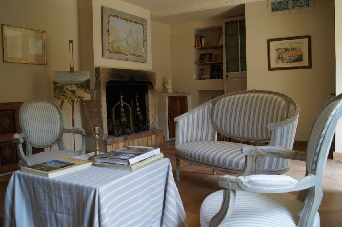 Un salon chaleureux avec une cheminée, des fauteuils à rayures et une table remplie de livres.