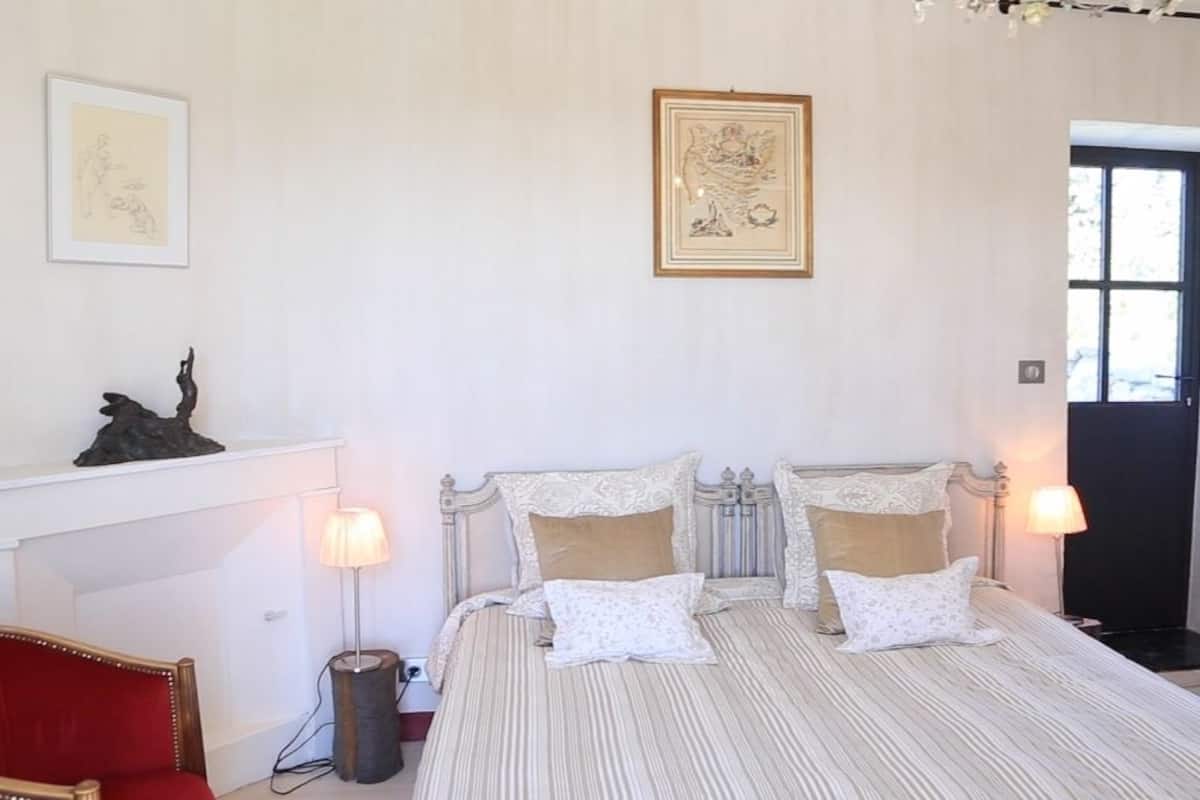 Een slaapkamer met een tweepersoonsbed, twee bedlampen, een rode stoel, een open haard en lijstwerken aan de wanden.