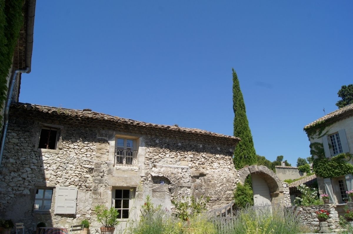 A stone building with a tiled roof, a balcony, and a tall tree in the background.