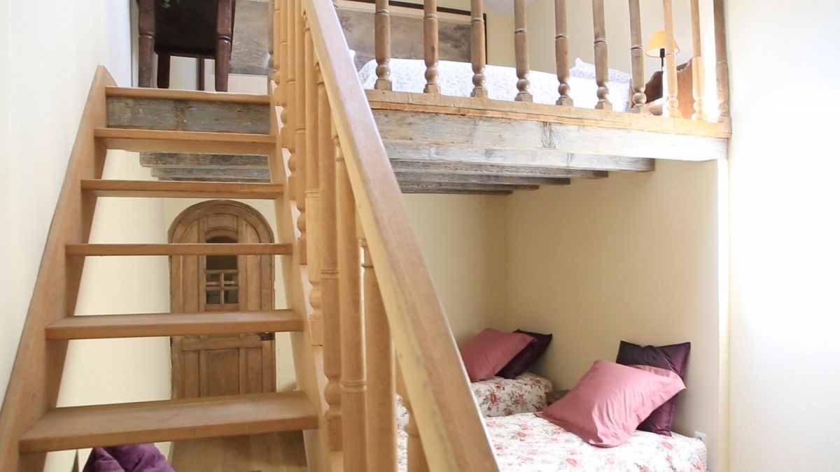 A wooden staircase leading to a loft bedroom with a bed and two pillows.