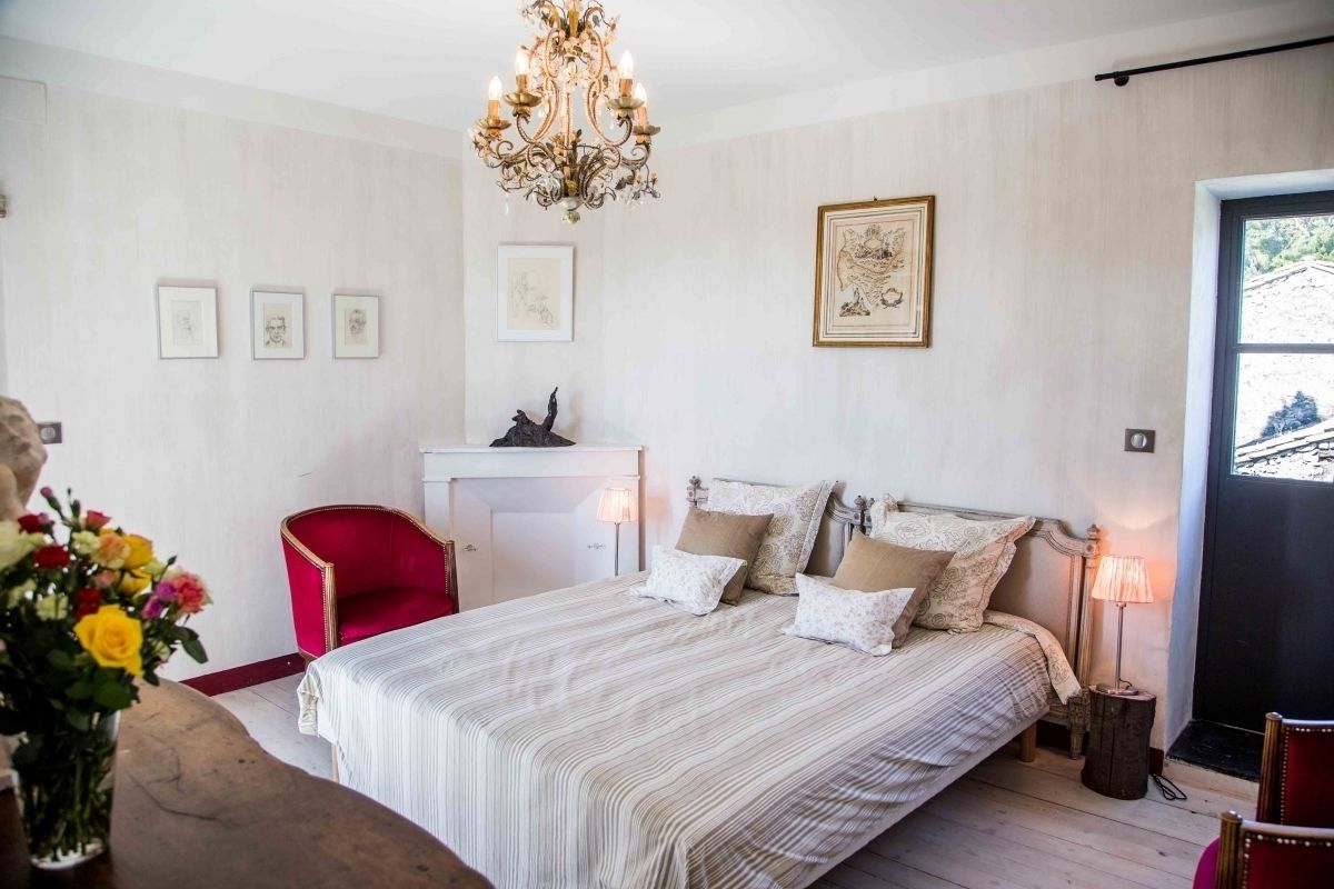 A bedroom with a bed, a desk, a chair, a chandelier, and a door.
