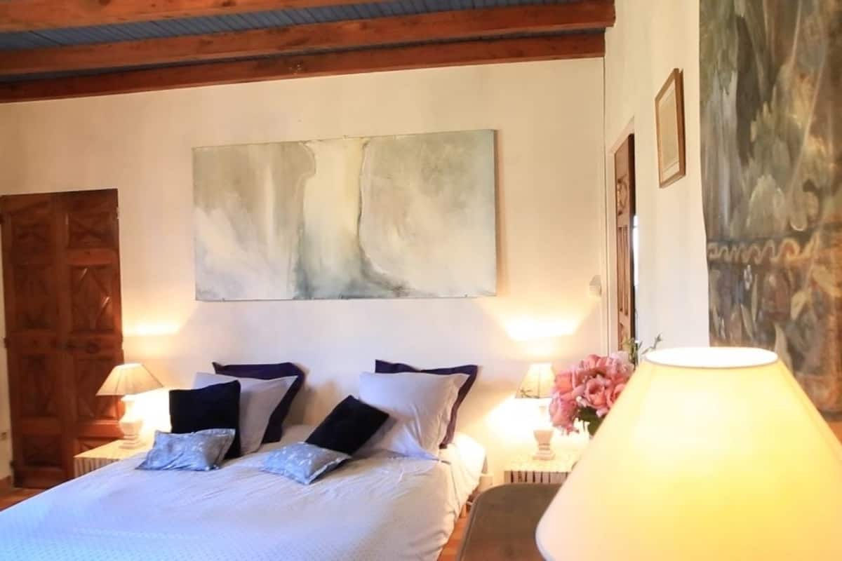 Een slaapkamer met een bed, twee nachtkastjes, een houten deur, een schilderij en een lamp.