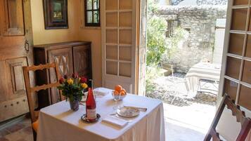 Un área de comedor con una mesa lista para dos comensales, un jarrón con flores, una botella de vino y un bol de fruta.