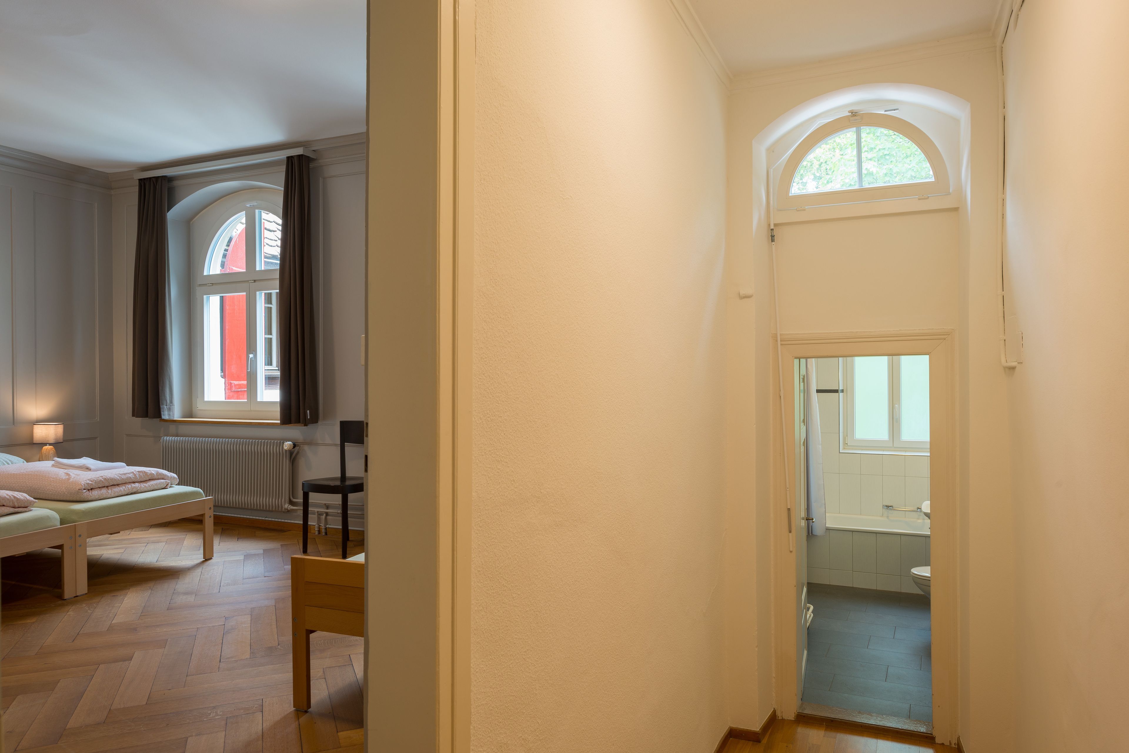 Un dormitorio con cama, una silla, un ventanal y vista al baño.