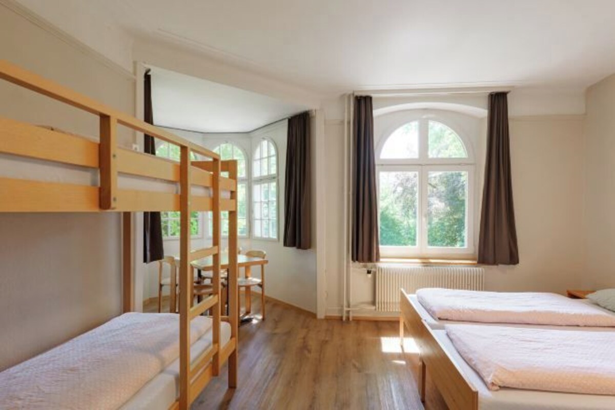A room with bunk beds, a desk, and a window with curtains.