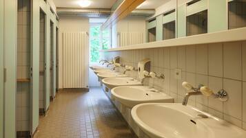 A public restroom with multiple sinks and stalls, a tiled floor, and a window providing natural light.