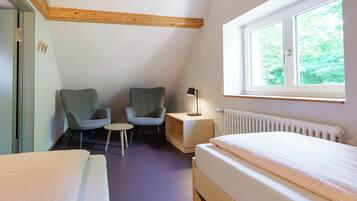 Ein Zimmer mit einem Bett, zwei Stühlen, einem kleinen Tisch, einer Lampe, einem Fenster und einer Heizung.