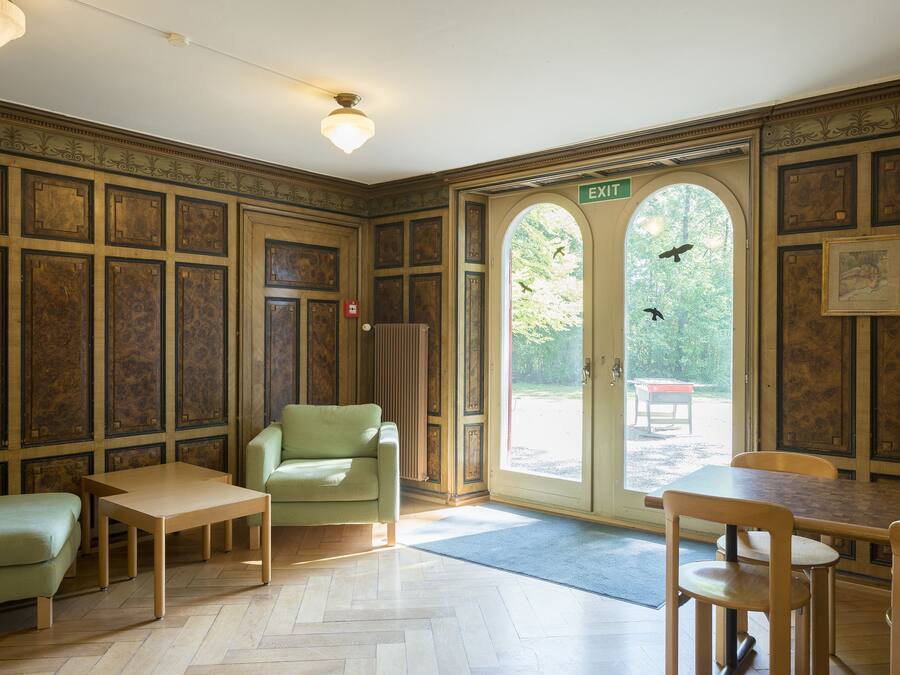 A room with a wooden herringbone floor, a green sofa, a wooden table, and a door leading outside.