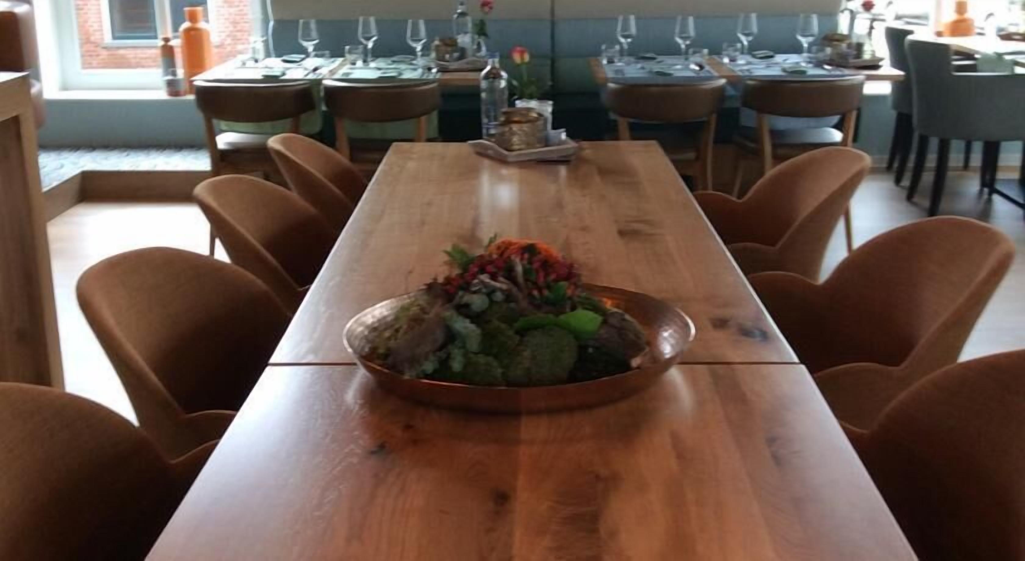 A long wooden table with a central serving dish containing food, surrounded by chairs.