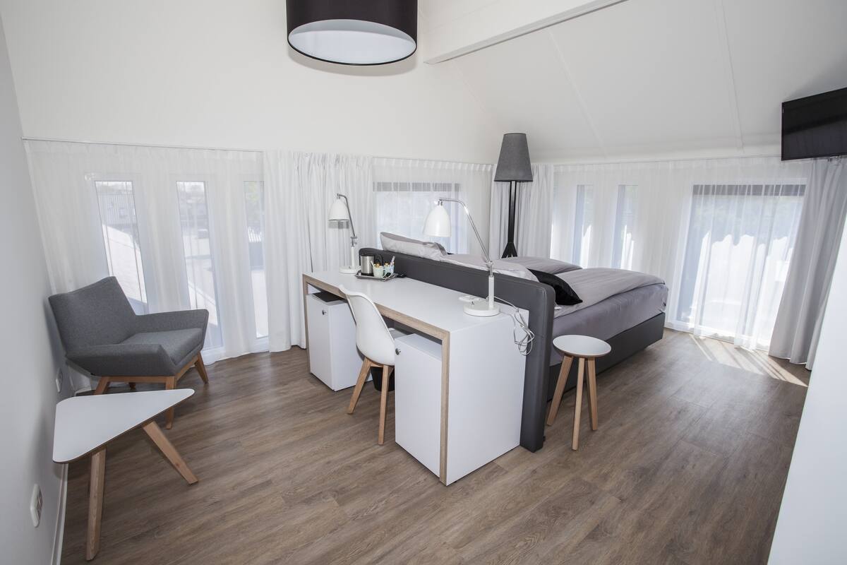A modern hotel room with a bed, desk, chair, and a TV mounted on the wall.
