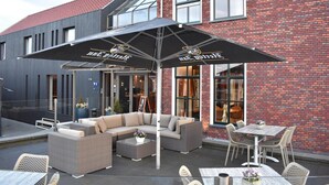 An outdoor seating area with a sofa, chairs, and tables, covered by a large umbrella. - Hotel Termunterzijl (Termunterzijl)