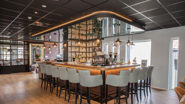 A bar area with a long counter, multiple stools, and a brick wall with shelves. - Hotel Termunterzijl (Termunterzijl)