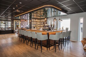 A bar area with a long counter, multiple stools, and a brick wall with shelves. - Hotel Termunterzijl (Termunterzijl)