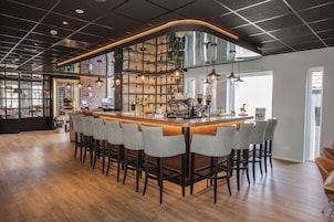 Uma área de bar com um balcão comprido, vários bancos e uma parede de tijolos com prateleiras.