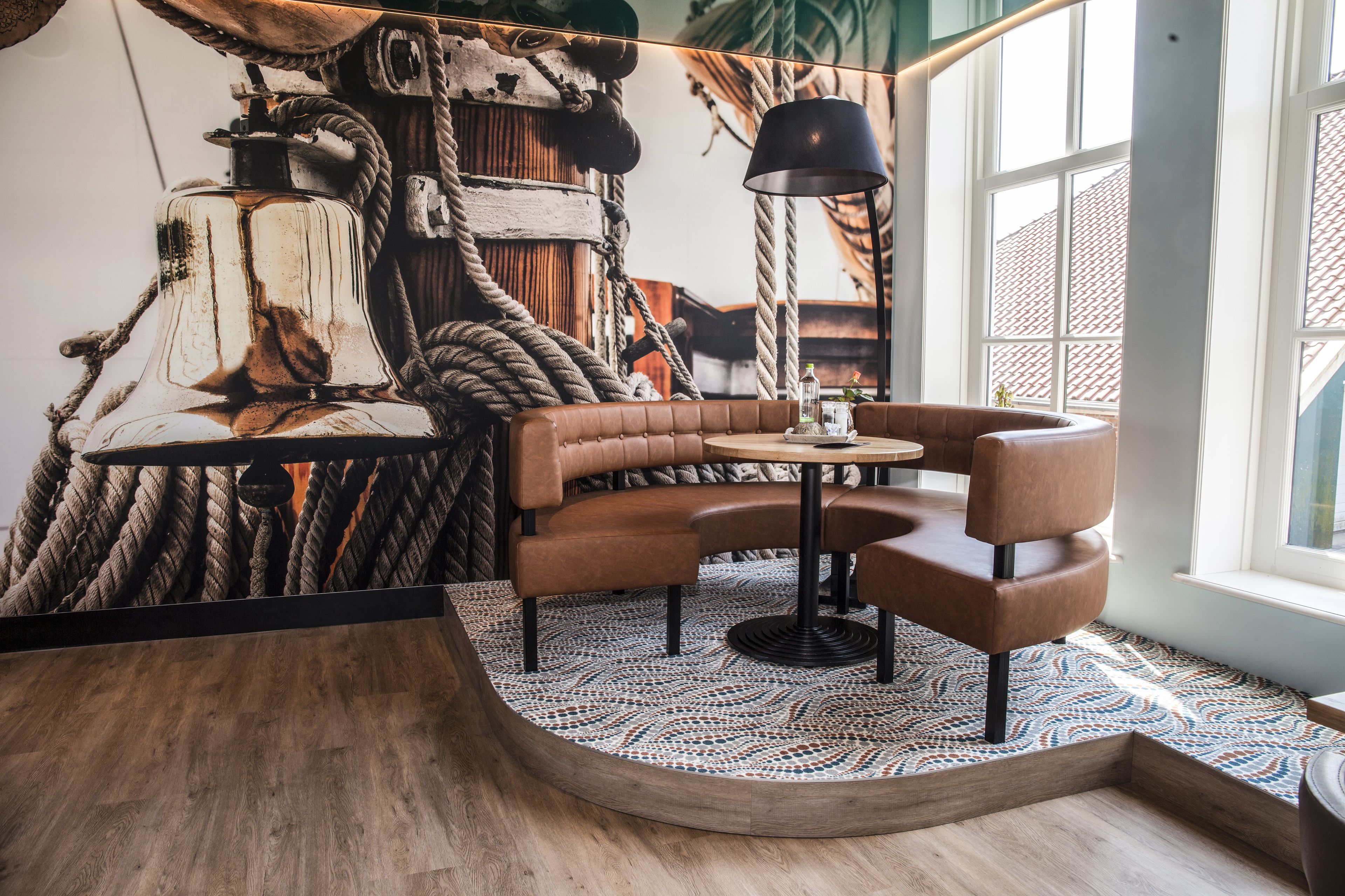 Un rincón acogedor con una mesa redonda, dos sillas, un tapete estampado y un mural de cuerdas y texturas de madera.