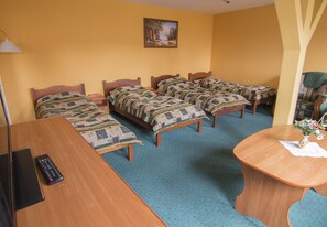 A hotel room with three wooden beds, a wooden desk, a remote control, and a painting on the wall.