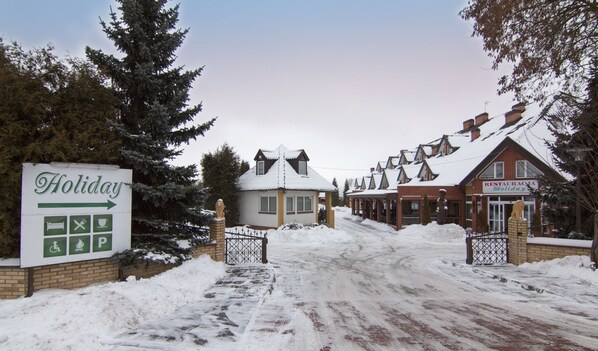 A snow-covered entrance to a holiday resort with a sign indicating amenities and directions.