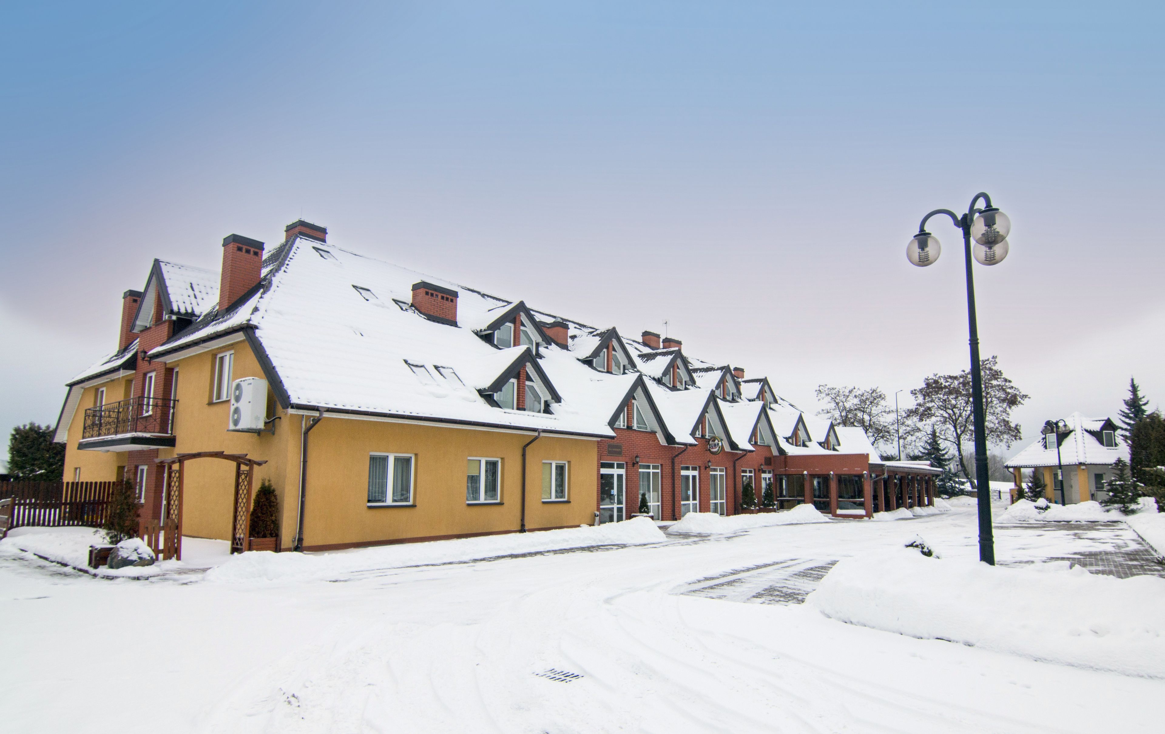 A row of yellow houses with snow-covered roofs and a street lamp.
