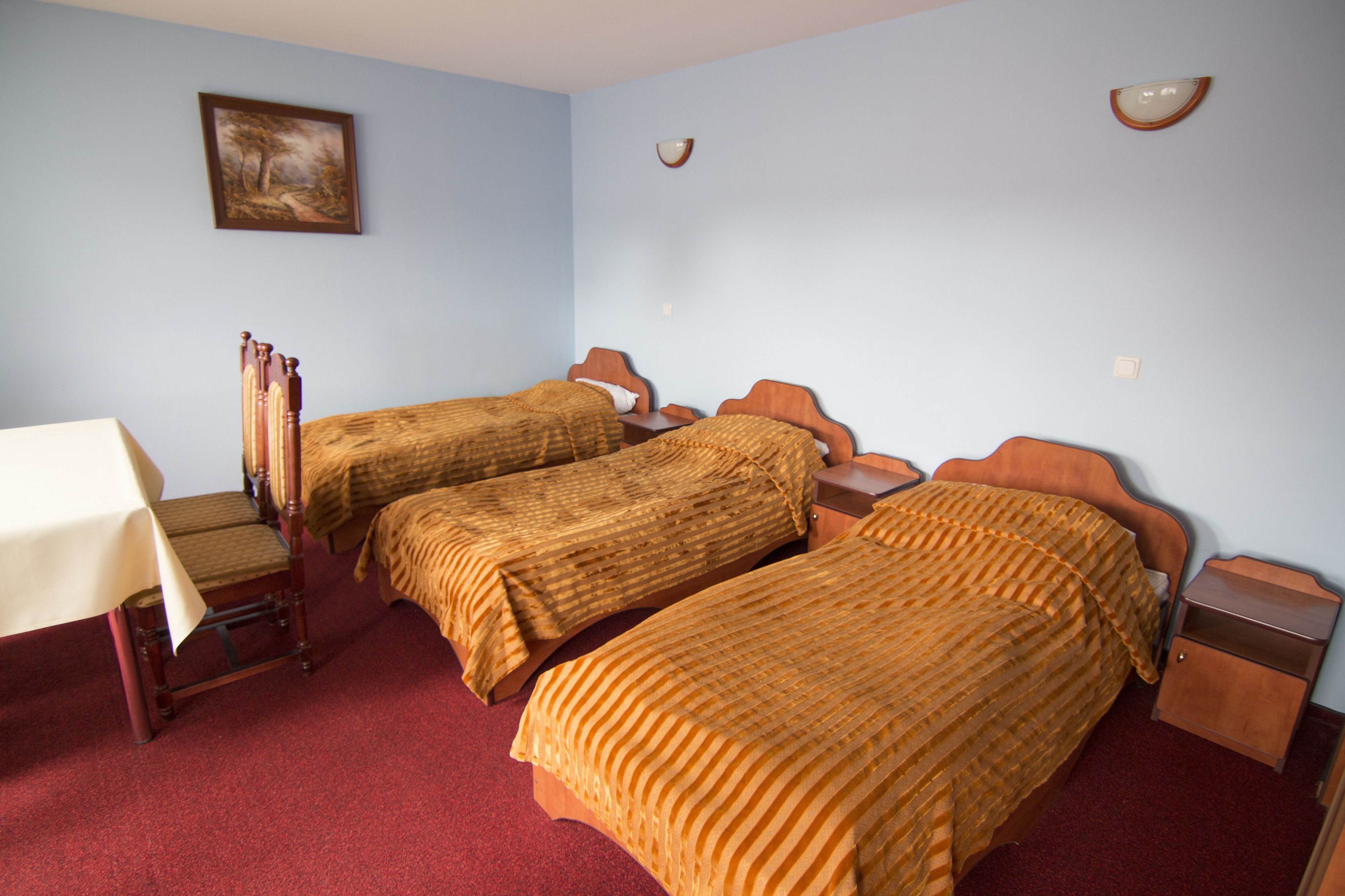 A room with two single beds, a wooden nightstand, a small table, and a painting on the wall.