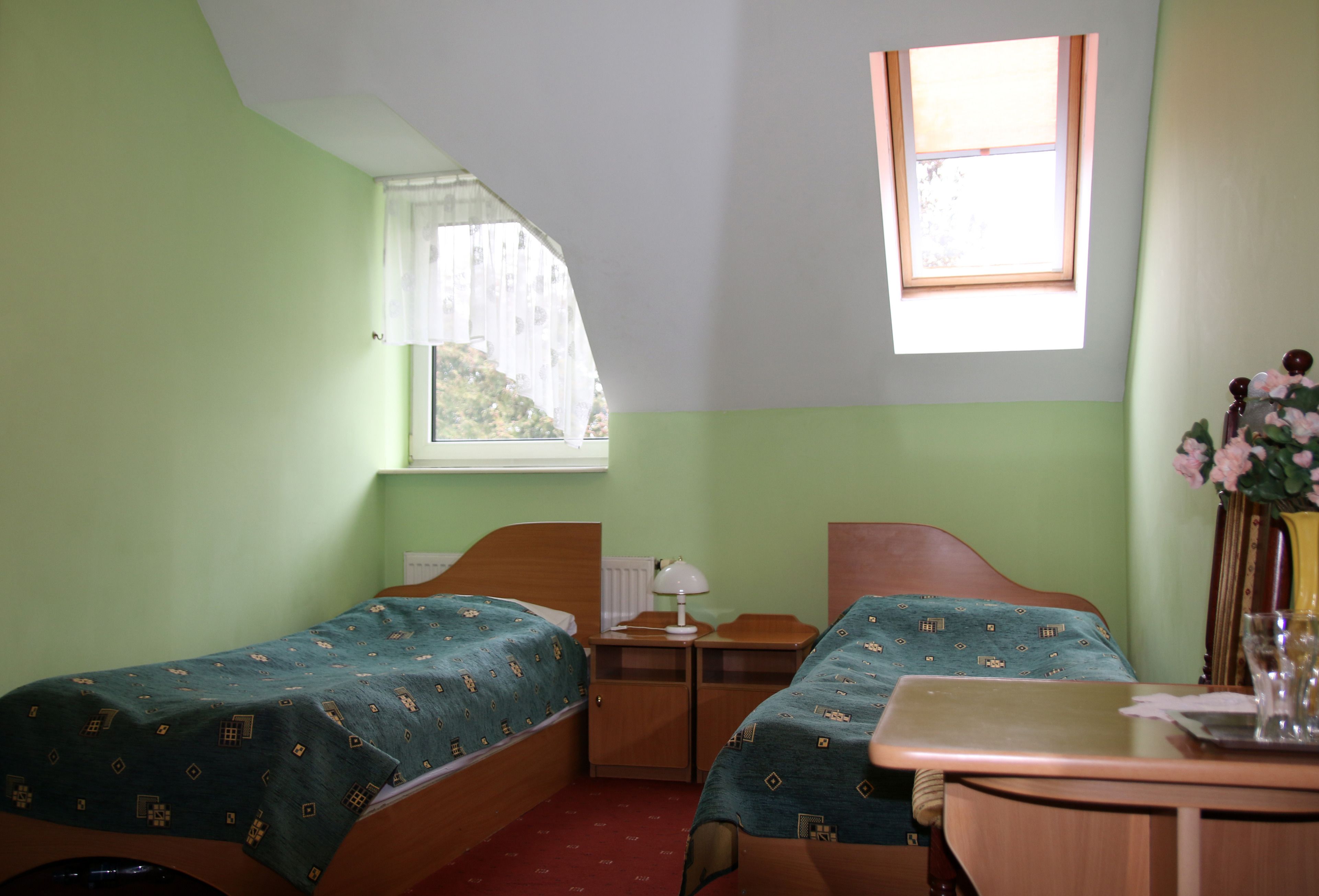 A room with two single beds, a small table, a window with a view, and a radiator.
