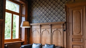Une pièce avec un radiateur en bois, un canapé en cuir noir, une table basse en bois et un papier peint à motifs.
