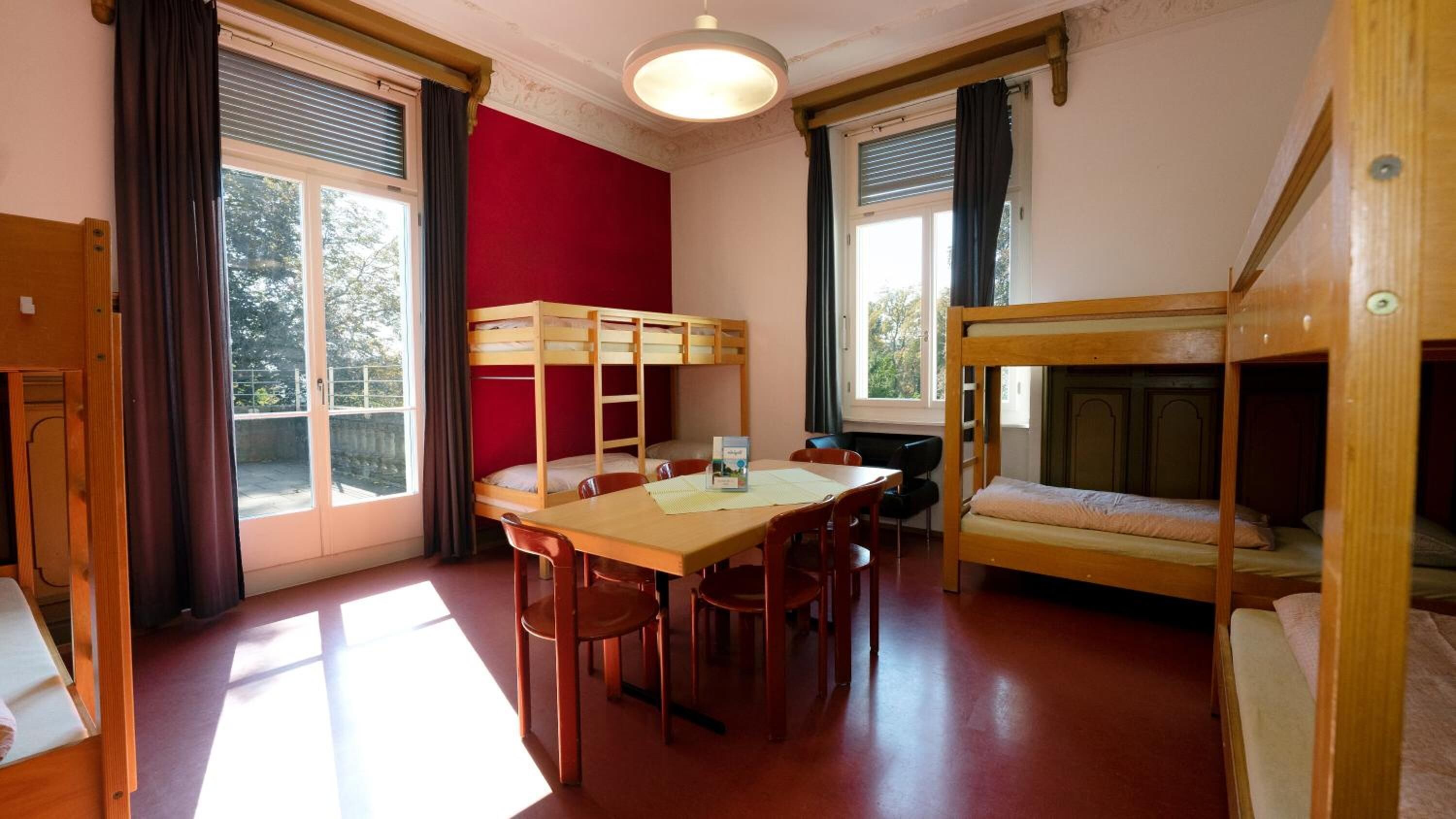 Un dormitorio con literas, una mesa, sillas y una ventana con cortinas.
