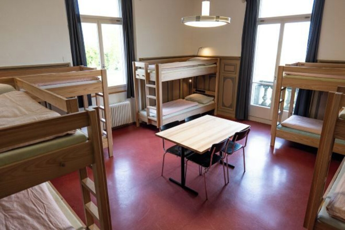 A room with bunk beds, a table, chairs, and a radiator.