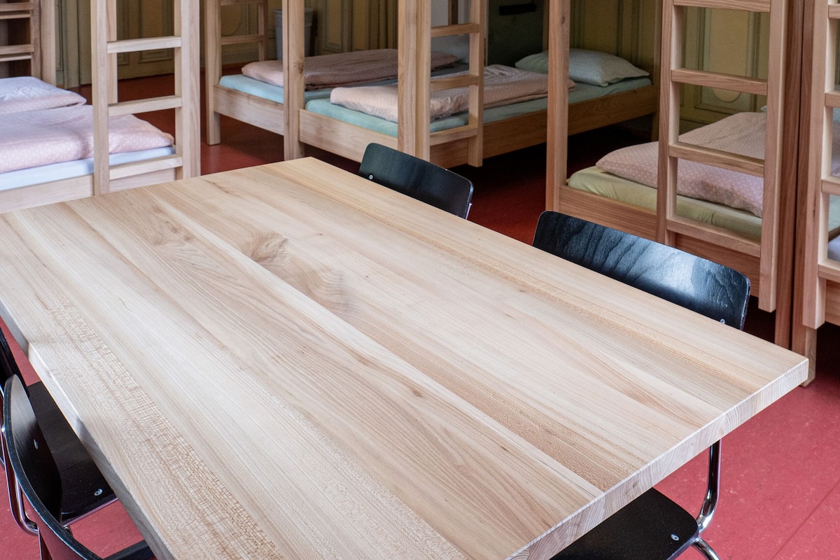 Une pièce avec des lits superposés, une table en bois et un luminaire fixé au plafond.