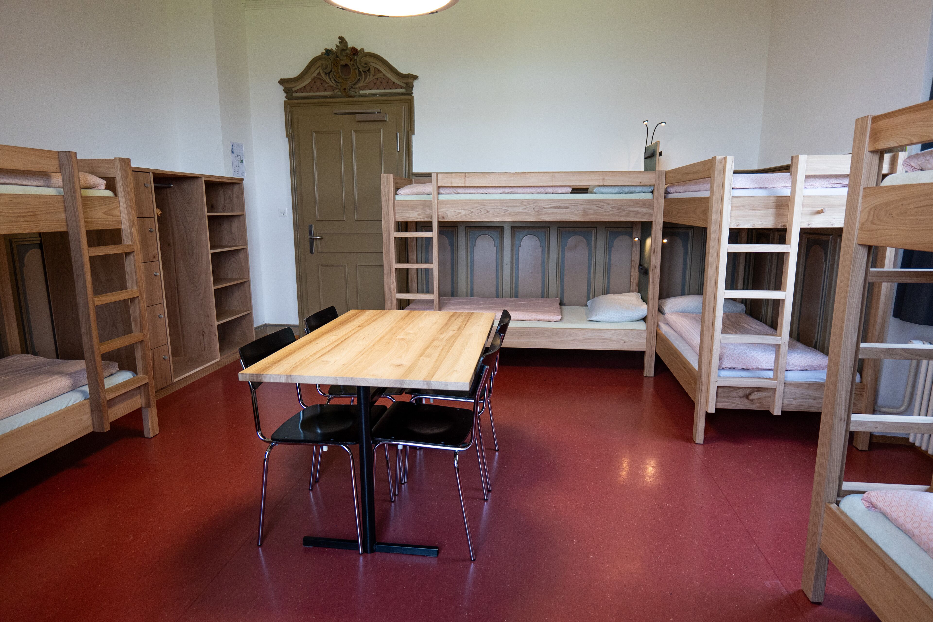 Dormitorio con literas, una mesa de madera y sillas, un armario y una puerta.