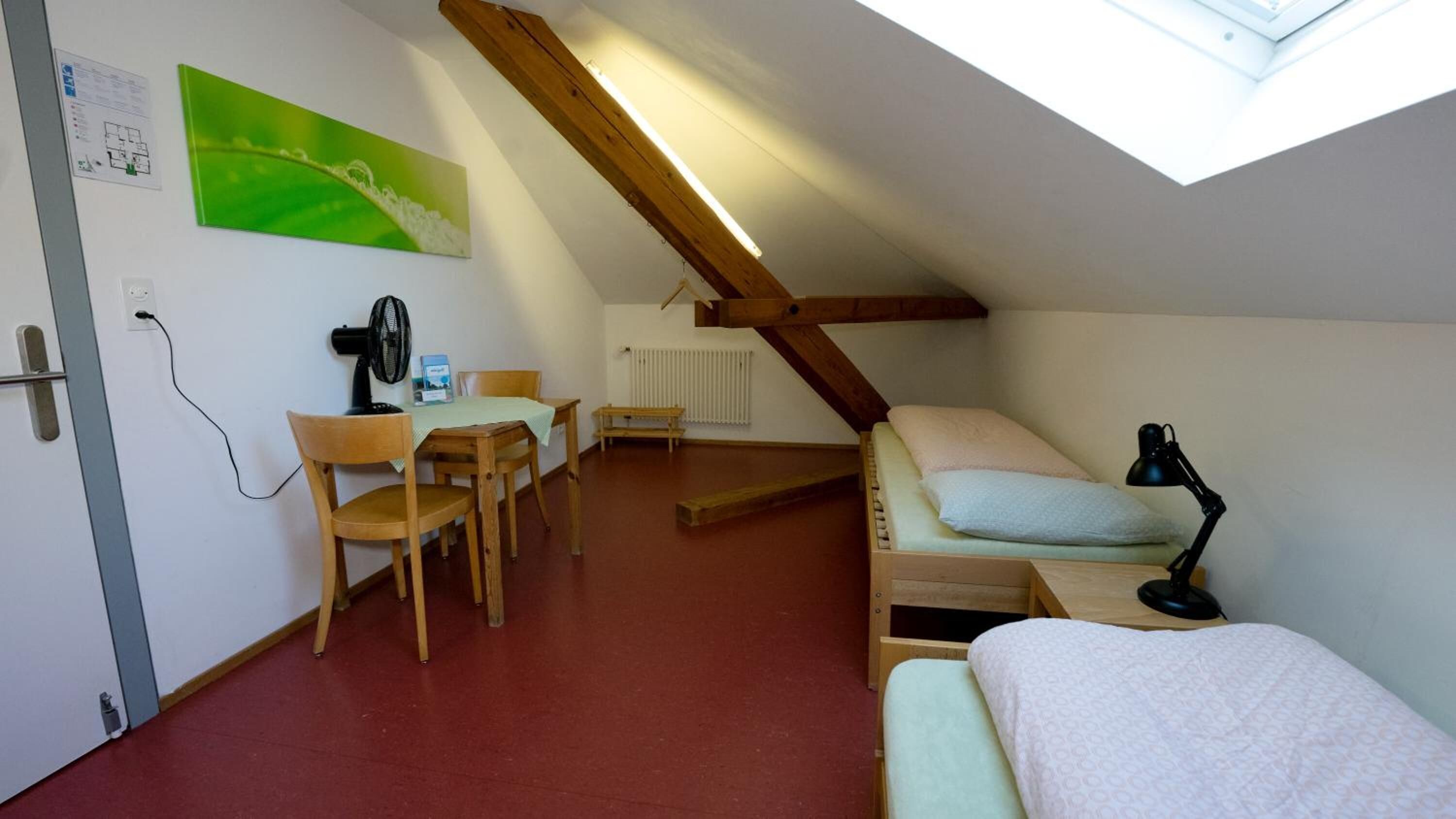 Une petite pièce agréable, avec un plafond en pente, un bureau avec une chaise, un lit et un radiateur.